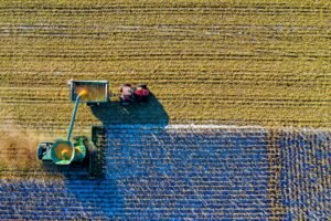 Drone captures vibrant aerial view of tractors harvesting corn in Minnesota field.