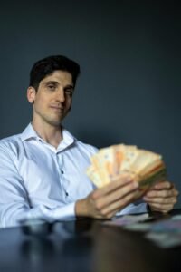 Businessman in a white shirt holding Argentine pesos with a confident expression indoors.